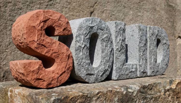 La palabra 'SOLID' esculpida en grandes letras de piedra rugosa, con la letra 'S' resaltada en rojo.
